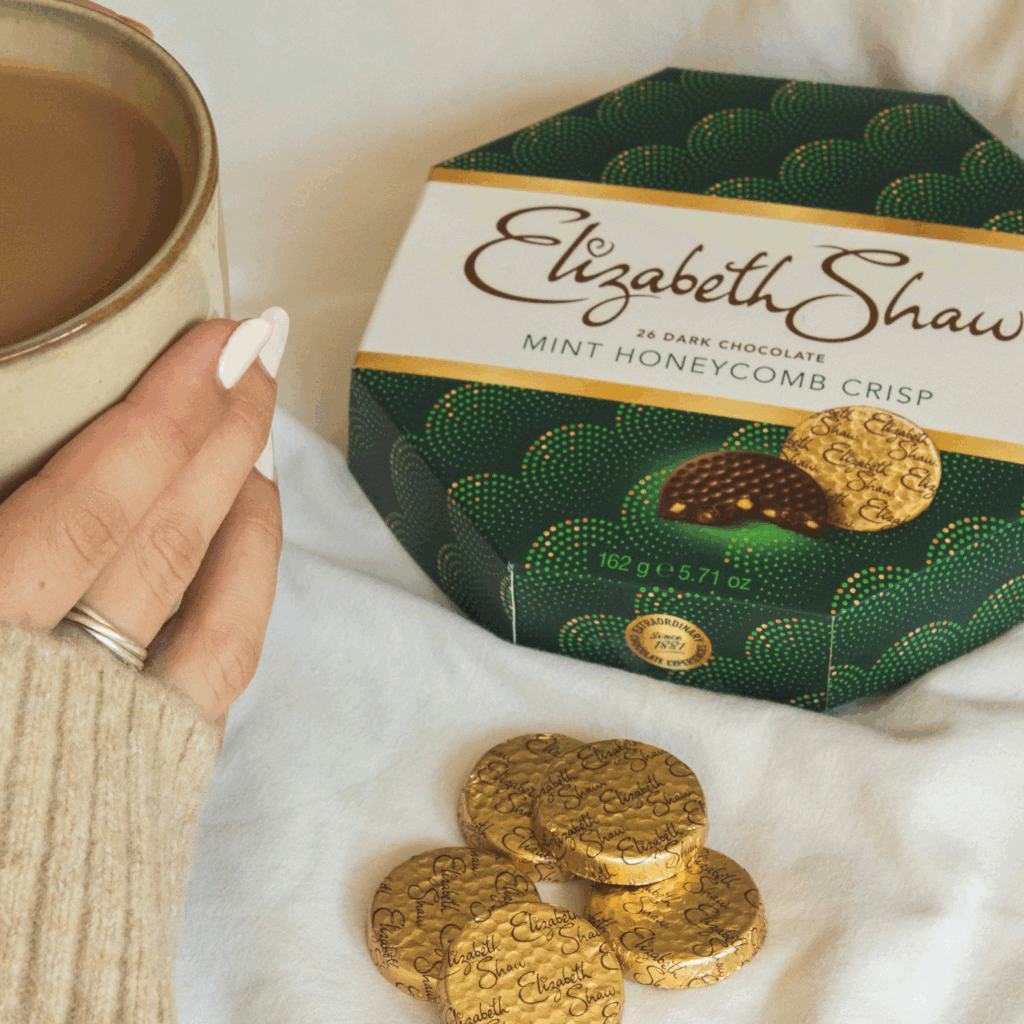 A hand holding a cup of tea and a box of Elizabeth Shaw Dark Mint Crisp