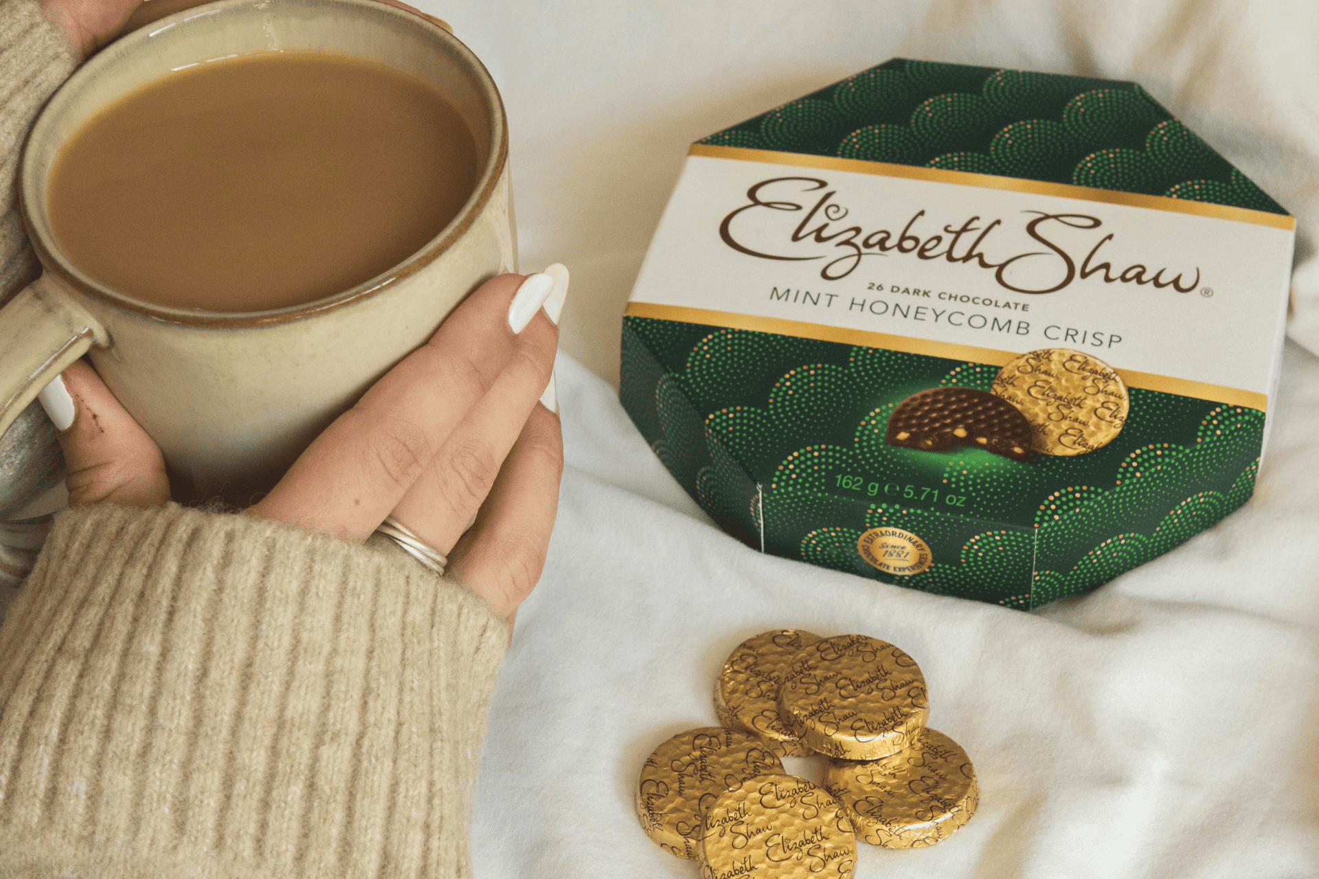 A hand holding a cup of tea and a box of Elizabeth Shaw Dark Mint Crisp