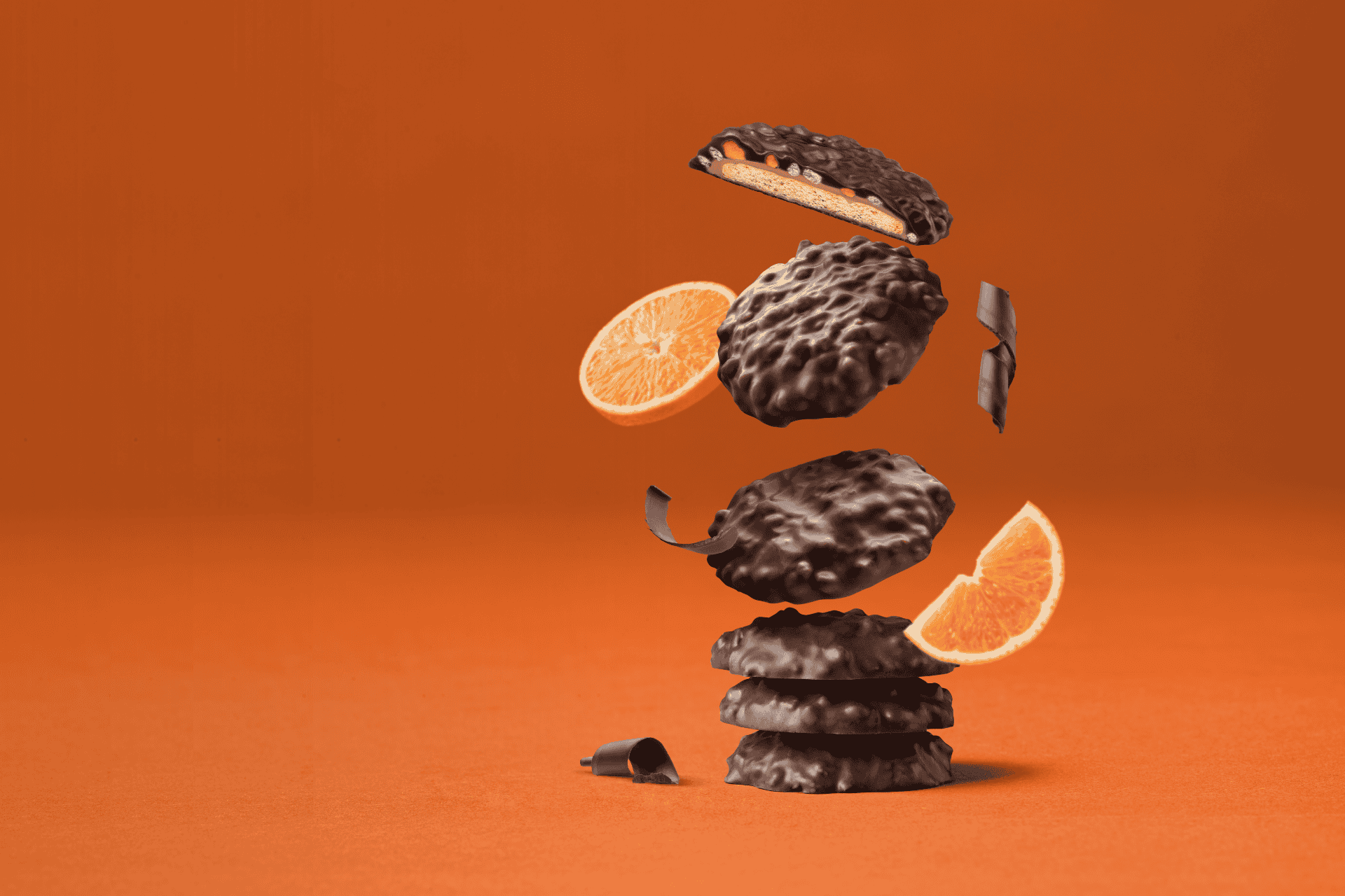 Dark chocolate biscuits falling in a stack onto an orange background. Orange slices fall alongside them.